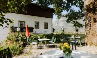 A charming café with green garden furniture and a red awning. In the background, there is a picturesque mountain panorama.