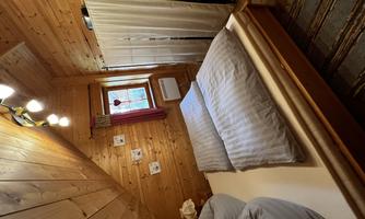 A cozy bedroom with wood paneling and a large bed. The atmosphere is warm and inviting with natural light.
