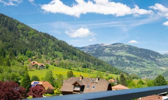 A picturesque view of green hills and mountains. In the foreground, charming houses and a radiant blue sky can be seen.