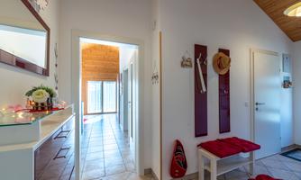 A bright hallway with a wooden ceiling and tiled floor. Hats are hanging on the wall, and a coat rack is available.