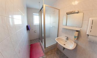A modern bathroom with a shower cubicle and a sink. The walls are tiled and a red carpet lies on the floor.