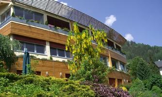A modern building with wooden cladding and large windows. Surrounded by lush greenery and colorful flowers.