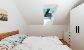 A cozy bedroom with a skylight and a large white wardrobe. The bedding has a floral design.