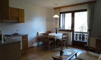 A cozy kitchen with wooden furniture and a dining table. Large windows let in plenty of light and offer a view outside.
