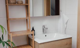 A modern bathroom with a wooden vanity and a large mirror. In the background, there is a bookshelf and a plant adds life to the room.
