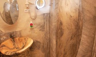 A modern bathroom with a stone shower cubicle and a stylish sink arrangement. The walls are clad with marbled material.