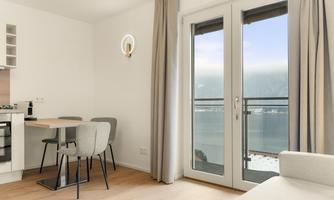 A modern room with a dining table and chairs. Large windows offer a view of the lake and mountains.