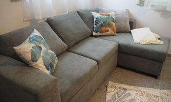 A modern gray sofa with colorful cushions is situated in a bright room. The carpet beneath has a floral pattern.