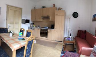 A cozy kitchen-living room with wooden furniture and a dining area. On the right side, there is a red sofa and a table.