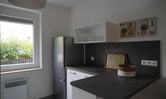 A modern kitchen with a refrigerator and plenty of storage space. Large windows provide ample daylight and a friendly atmosphere.