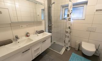 A modern bathroom with a shower, a sink, and a toilet. The walls are brightly tiled and there is a large window.