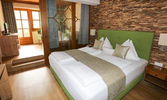 A cozy hotel room with a large double bed and modern wood design. The room has large windows that let in plenty of light.