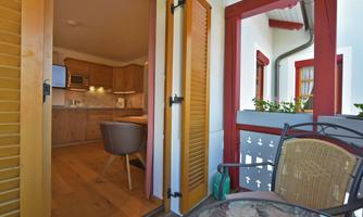 A cozy balcony with wooden chairs and a view of a modern kitchen. The doors are open and let in a lot of light.