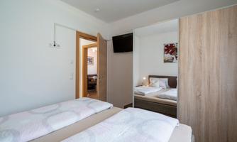 A comfortable bedroom with two single beds and a television. The walls are bright and there is access to an adjoining room.