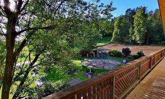 A green landscape with trees and a paved patio. In the background, numerous play opportunities and a lawn can be seen.