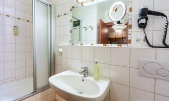 A modern bathroom with a shower, a sink, and a large mirror. The walls are brightly tiled, and there are decorative elements in warm colors.
