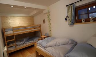 A cozy bedroom with a bunk bed and a single bed. The walls are bright, and there is natural light coming through the window.