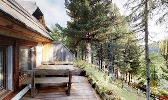 A wooden terrace with a table and chairs, surrounded by tall, green trees. The view offers a calm, nature-friendly atmosphere.