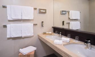 A modern bathroom with a double sink and large mirrors. Fresh towels and toiletries are neatly arranged.