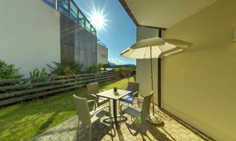 A cozy outdoor area with a table and chairs under a sun umbrella. The sun is shining brightly and there is a green lawn in the background.