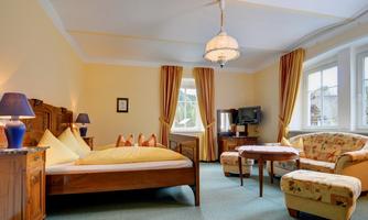 A cozy bedroom with a large bed and an elegant armchair. The walls are painted yellow, and the room is bright and inviting.