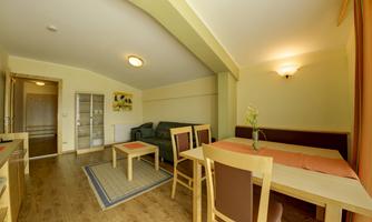 A bright living room with a cozy couch and a dining table. The walls are painted in a soft yellow hue, and the floor is made of wood.