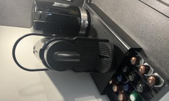 A black coffee machine with space for capsules stands on a countertop. Next to the machine, there is a water tank.
