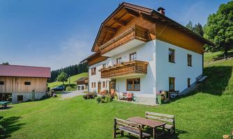 A charming country house with a balcony in a green setting. In the foreground, there is a wooden table on a meadow.