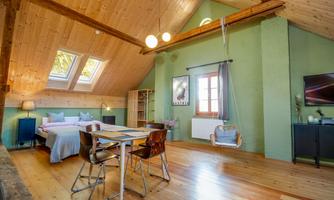 A bright, modern room with wooden ceilings and large windows. It has a bed, a dining table, and a cozy seating area.