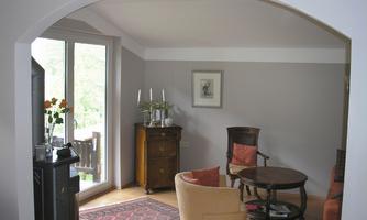 A cozy living space with a round table and comfortable chairs. Large windows provide plenty of daylight and a view of the outdoors.