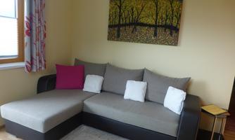 A cozy living area with a gray sofa and colorful cushions. A painting featuring trees and yellow leaves hangs on the wall.