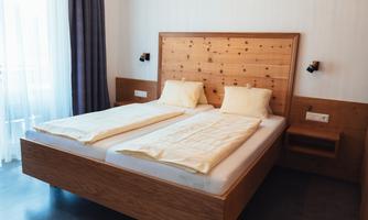A modern bedroom with a wooden double bed. The walls are bright and the windows let in plenty of light.