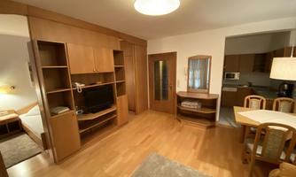 A bright and cozy apartment with wooden shelves and a dining table. The room is well-furnished and radiates an inviting atmosphere.