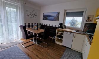 A modern kitchen with a dining table and chairs. Bright walls and large windows provide plenty of daylight.