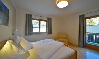 A cozy bedroom with a double bed and a bright decor. The windows offer a view outside, and there is an armchair for relaxation.