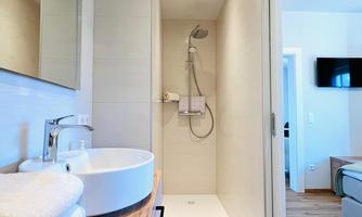 A modern bathroom with an open shower and a sink and toilet. White walls and wooden details create a bright, inviting atmosphere. Electric heating.