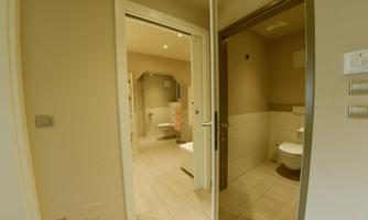 A modern bathroom area with doors leading to two separate toilets. The walls are in neutral colors and the floor is tiled.