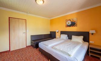 A cozy hotel room with two single beds and orange walls. There is a couch and a picture on the wall.