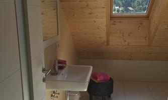 A modern bathroom with wooden ceilings and a large window. There is a striped rug on the floor and a small stool in the corner.