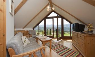 A cozy living room with wooden furniture and a large window that offers a beautiful view. The room has a modern television and a friendly atmosphere.