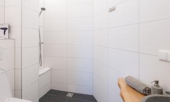 A modern bathroom with white tiles and a shower. The wooden vanity with an elegant sink completes the design.