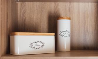 Two decorative storage jars on a wooden shelf. One is rectangular, the other is cylindrical, both with a wooden lid.