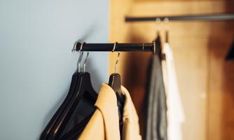 A clothes hanger with various garments hangs on a wall. In the background, more clothing items are visible.