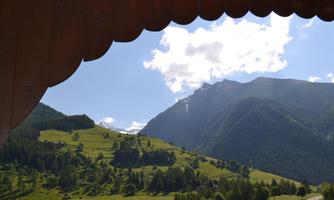 A picturesque mountain valley with green meadows and tall mountains. The sky is blue with scattered white clouds.
