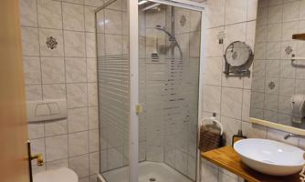 A modern bathroom with a shower cabin and a sink on a wooden shelf. The walls are tiled with light tiles.