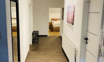 A bright hallway with white walls and a modern design. In the background, there are doors to the rooms, as well as a mirror and a small table.