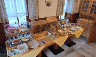 A rich breakfast buffet with cold cuts, cheese, fresh fruit, and various beverages. The tables are set with yellow cloths, creating an inviting atmosphere.