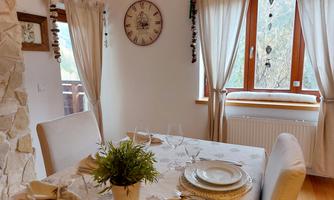 An inviting dining area with a table, lovingly set with dishes and cloth napkins. Large windows provide plenty of daylight and a view of the greenery.
