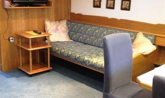 A cozy living space with a sofa, a table, and chairs. On the wall hangs a television and there are decorative pictures.