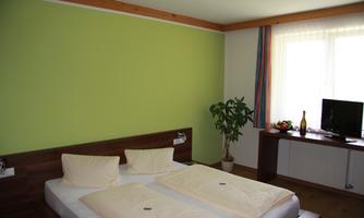 A cozy bedroom with a double bed and a green wall accent. Next to the bed, there is a small table with a bottle and fruit, and a television is also available.